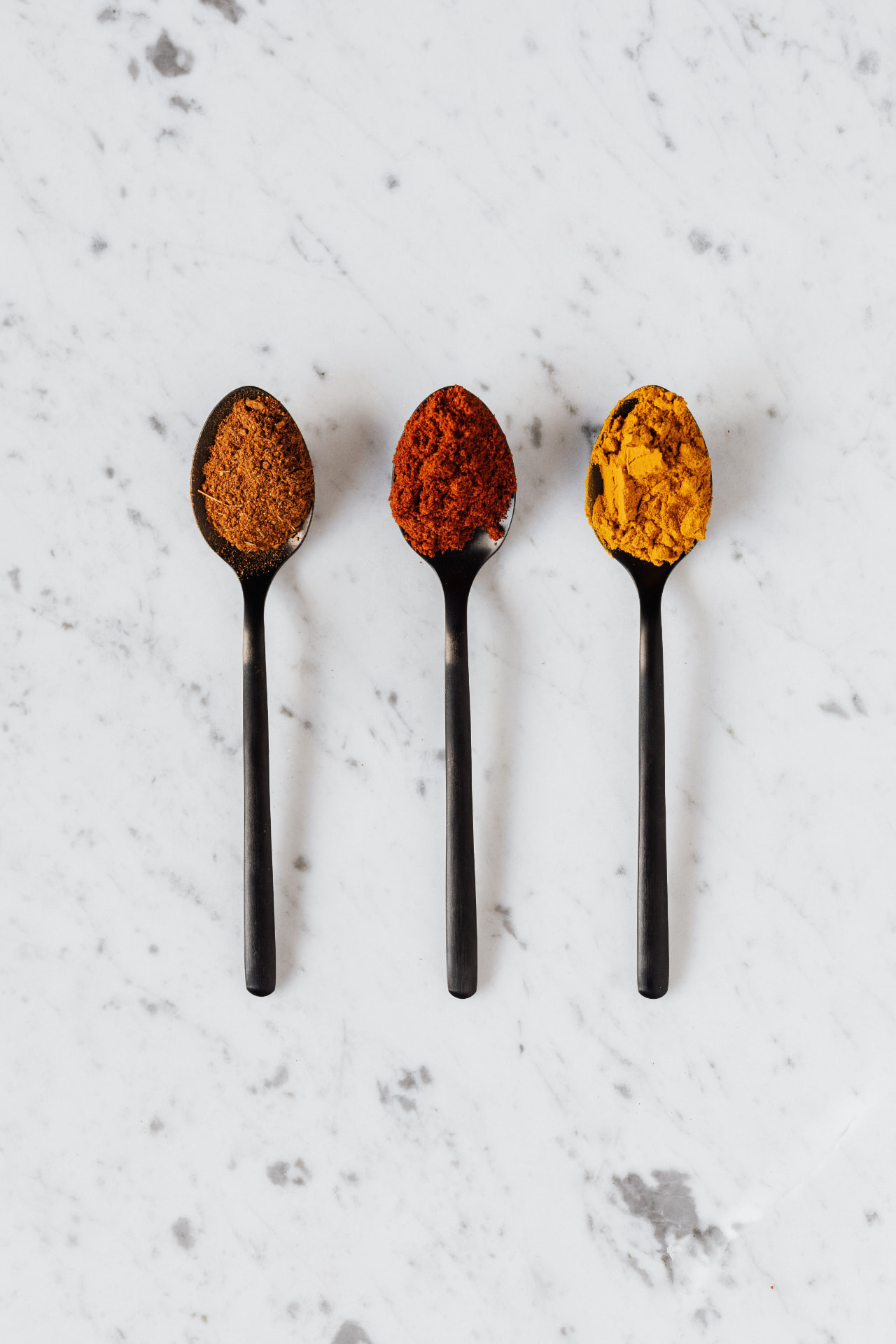 Three spoons filled with warm-toned spices