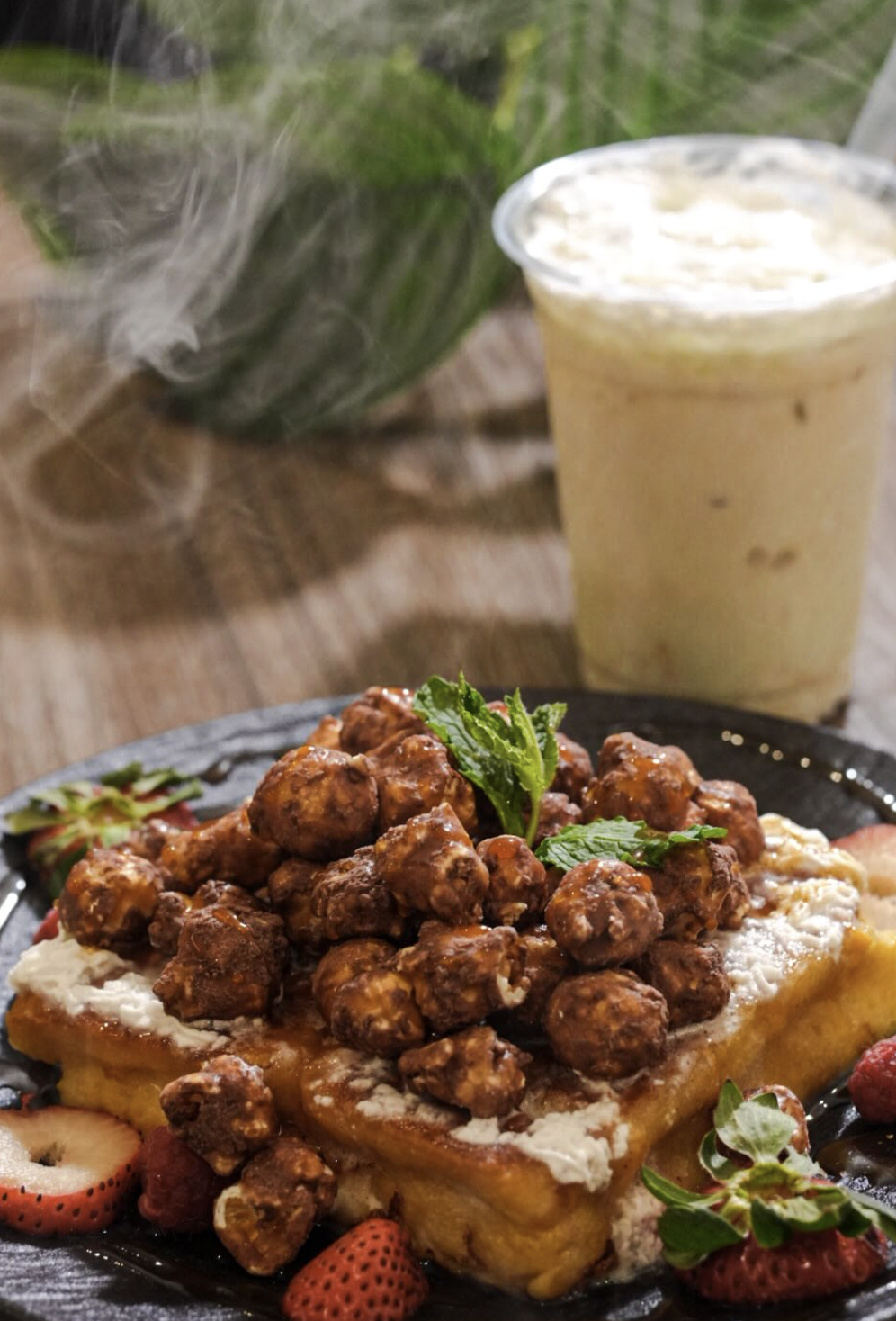Brunch waffles loaded with candied bites, berries, mint, and an iced latte