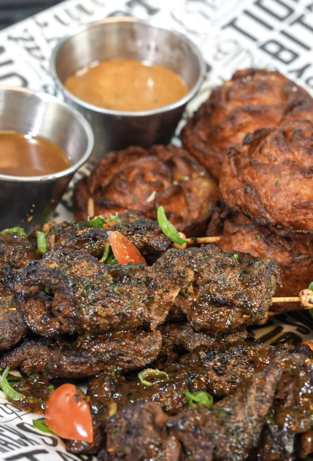 Suya beef skewers plated with puff puff and two house sauces