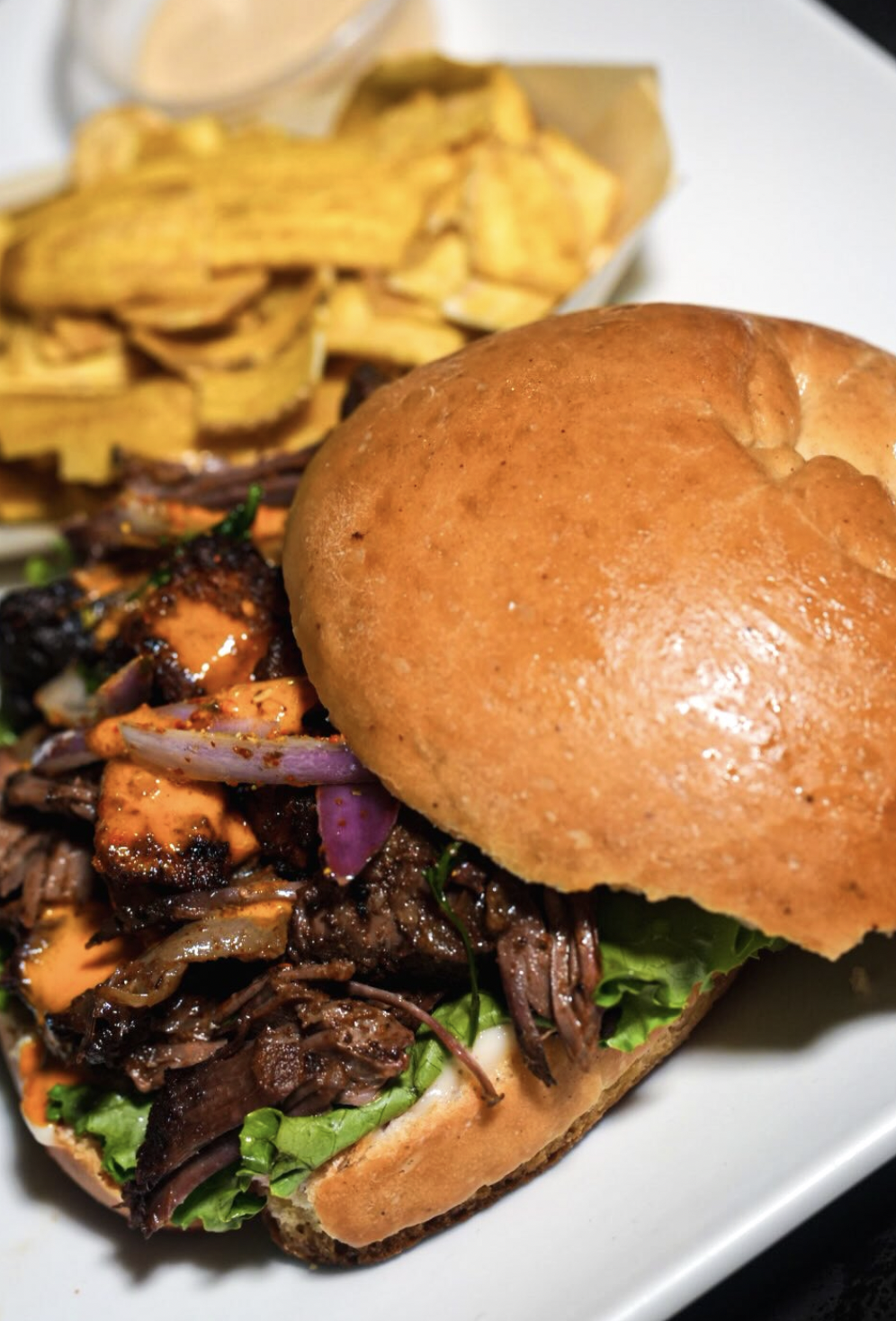Close crop of FloJoe's braised beef slider with glossy bun, greens, and sauce