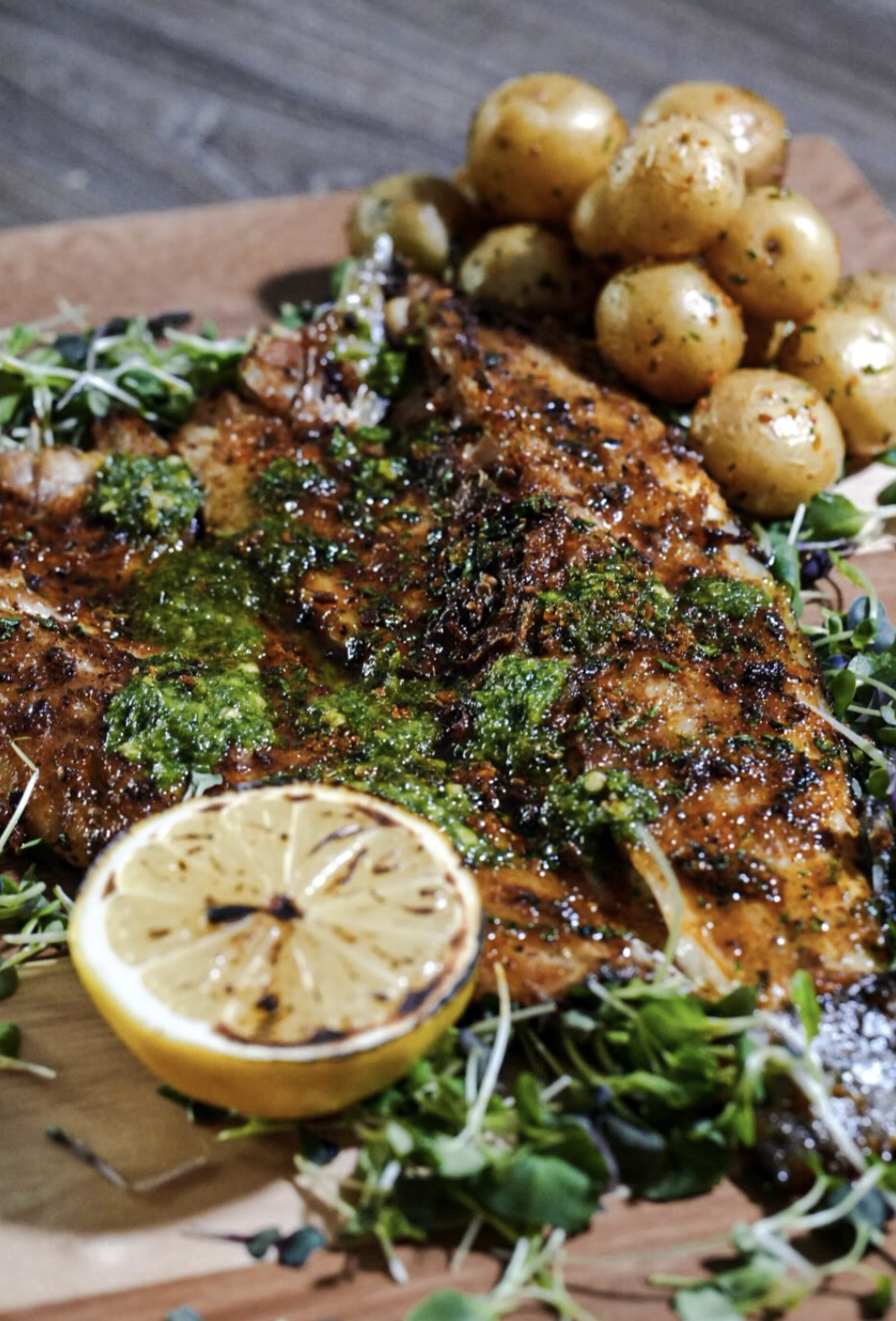 Herb-crusted whole fish served with roasted baby potatoes, charred lemon, and greens
