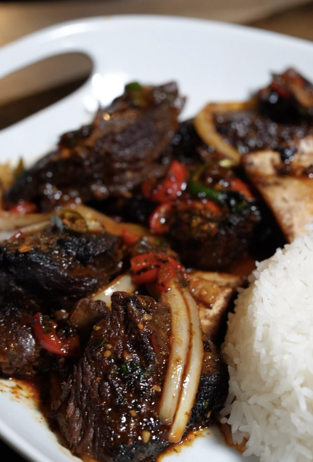 Braised beef over white rice with peppers, onions, and glossy sauce