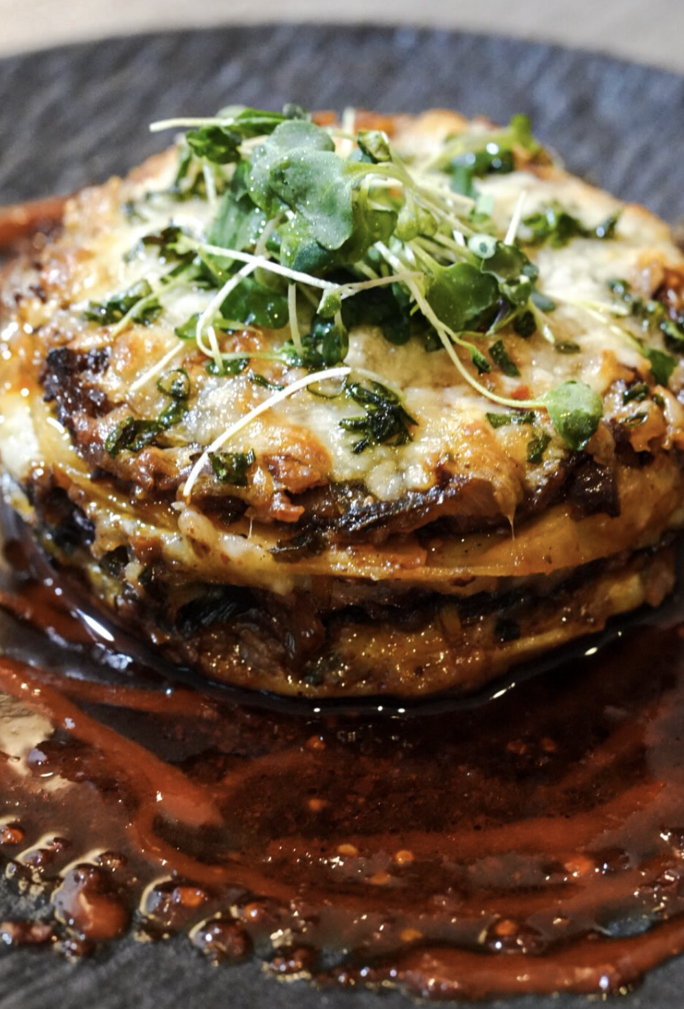 Layered plantain bake with melted cheese, greens, and pepper glaze