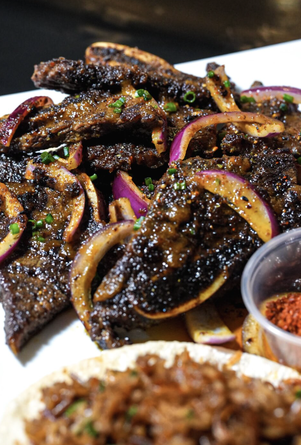 Close crop of FloJoe's suya platter with charred beef strips and onions