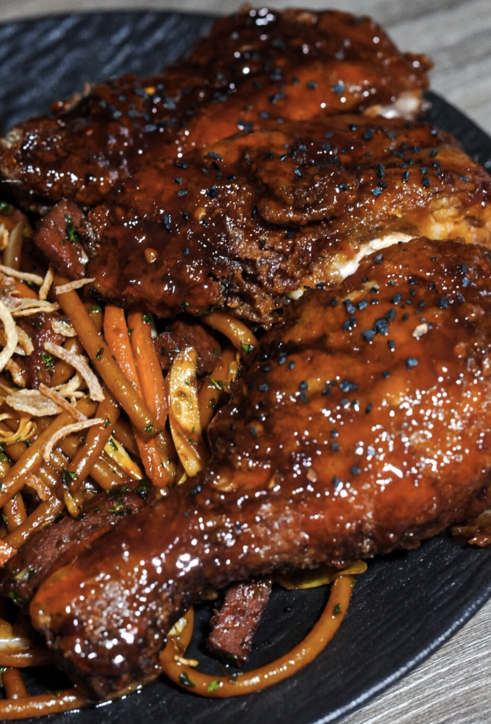 Glazed chicken legs over noodles with carrots and crisp garnishes
