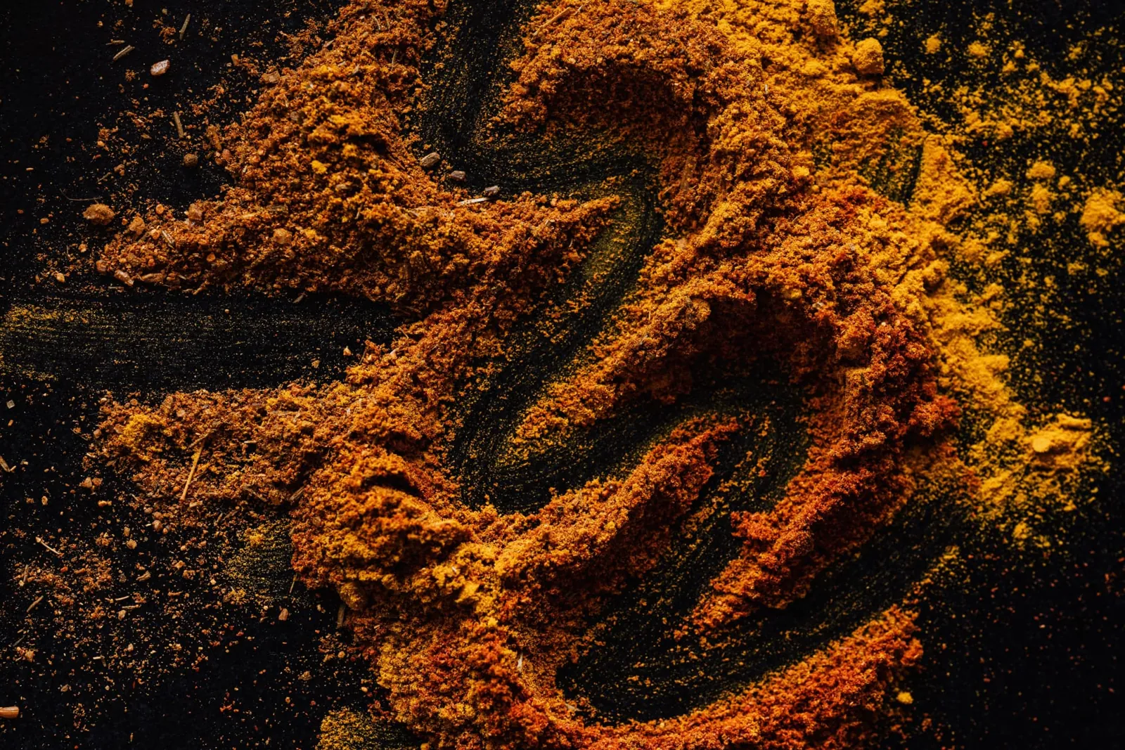 Red and golden spices scattered across a dark surface