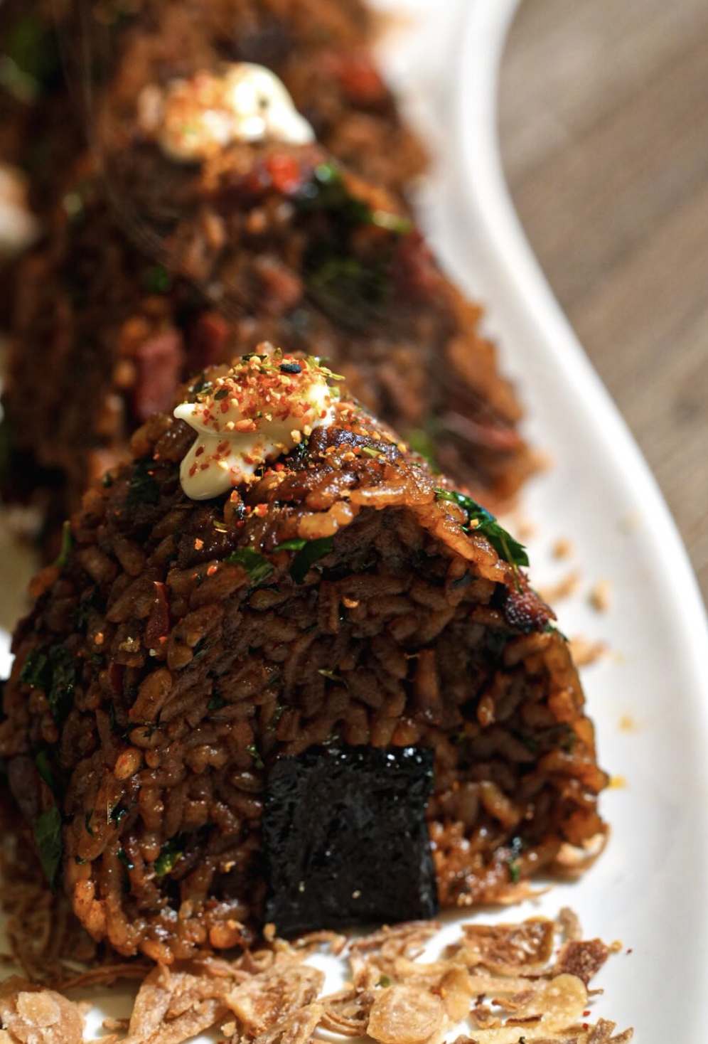 Close-up molded jollof rice with braised beef, greens, cream, and crisp garnish