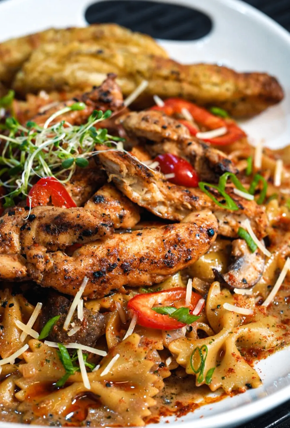Grilled chicken served over farfalle pasta with peppers, parmesan, and microgreens