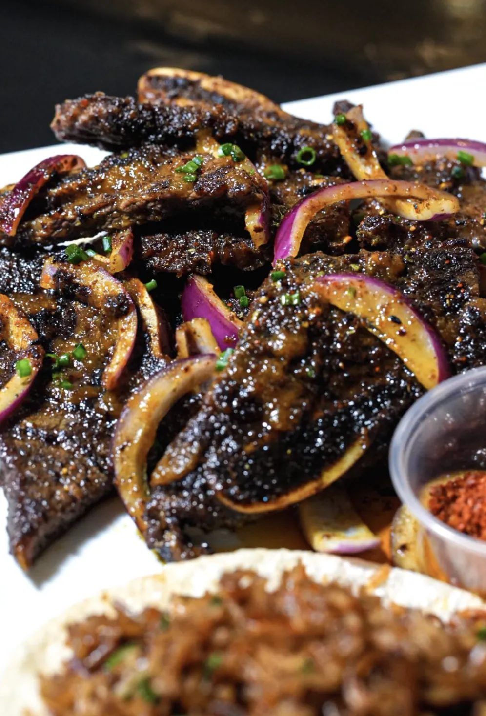 Close crop of FloJoe's suya platter with charred beef strips and onions