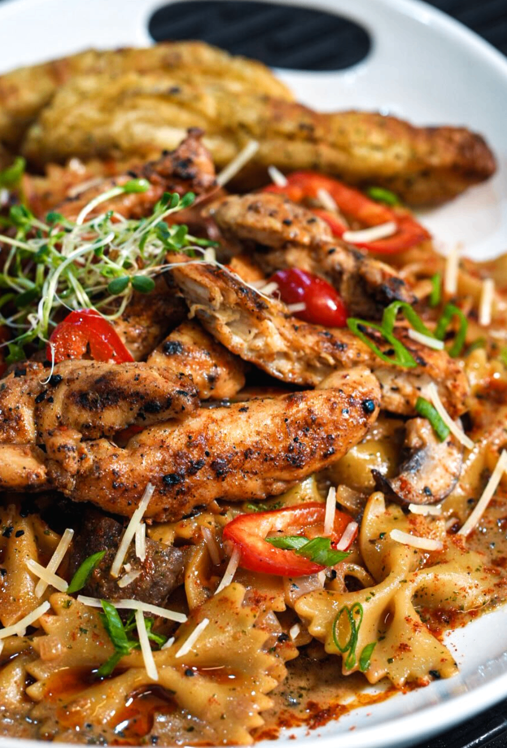 Grilled chicken served over farfalle pasta with peppers, parmesan, and microgreens