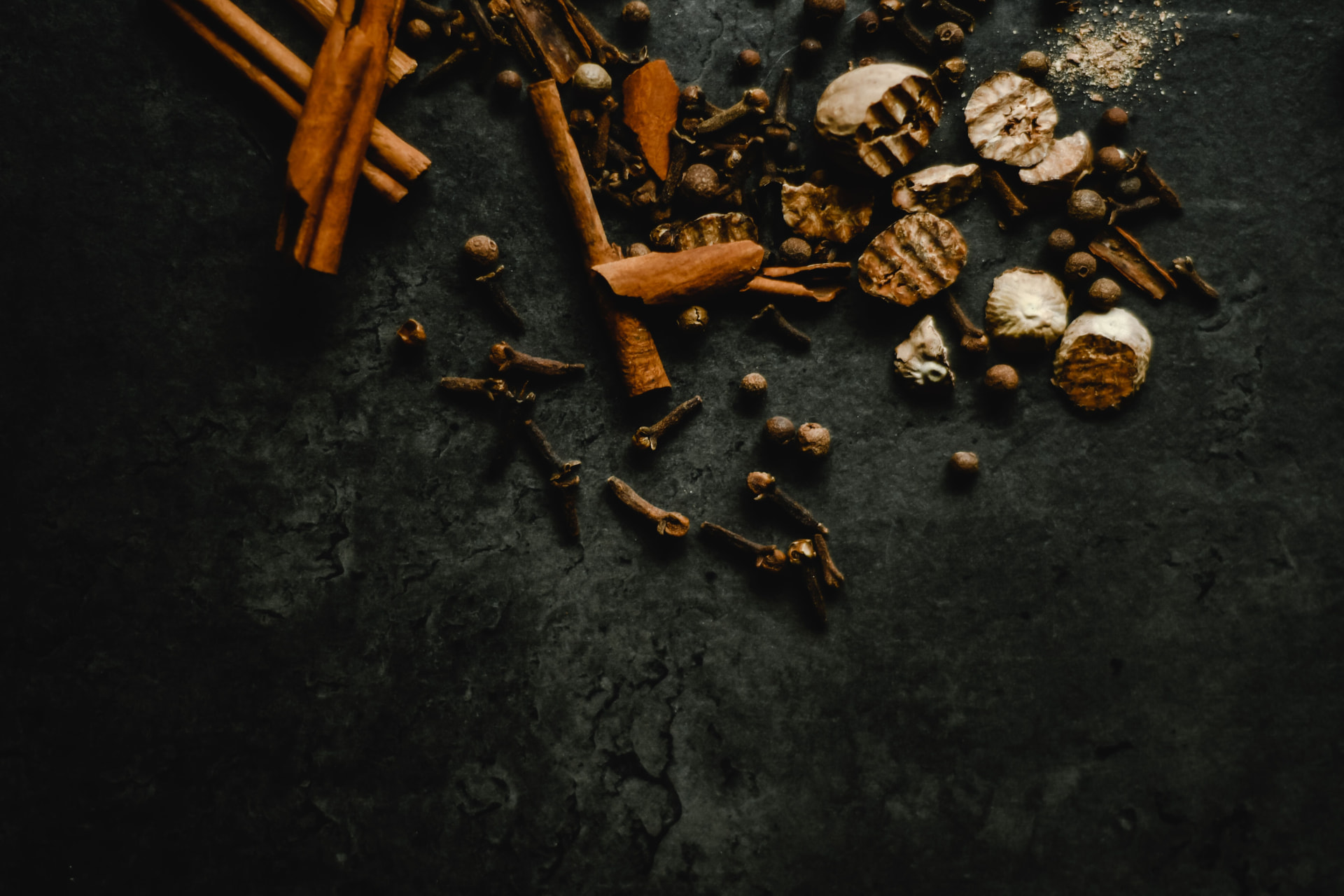 Cinnamon, cloves, and whole spices against a dark textured surface