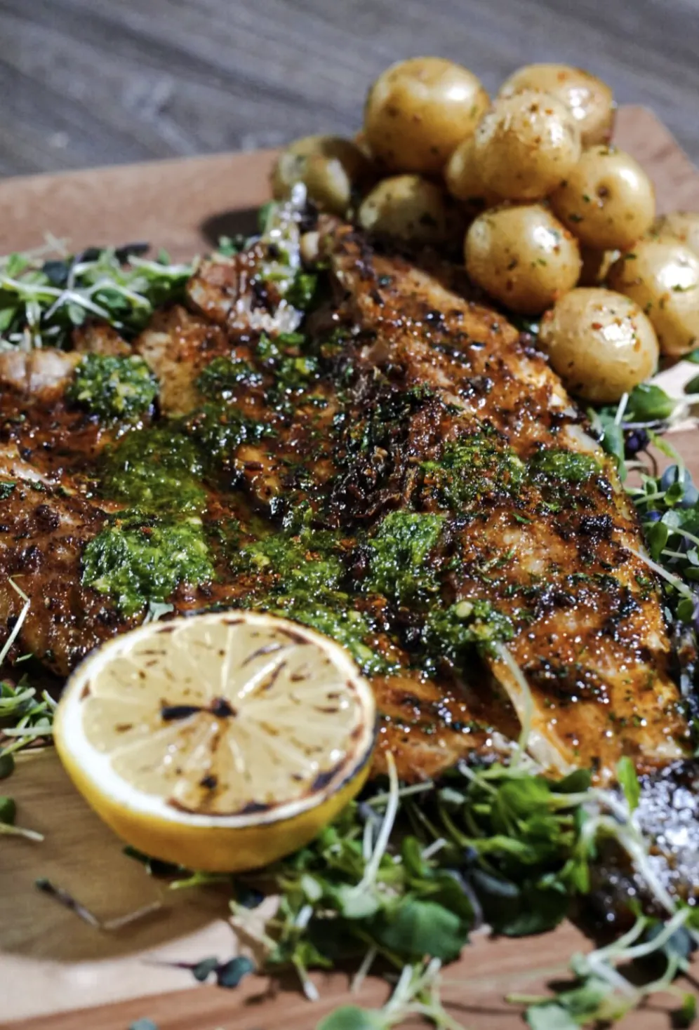 Herb-crusted whole fish served with roasted baby potatoes, charred lemon, and greens