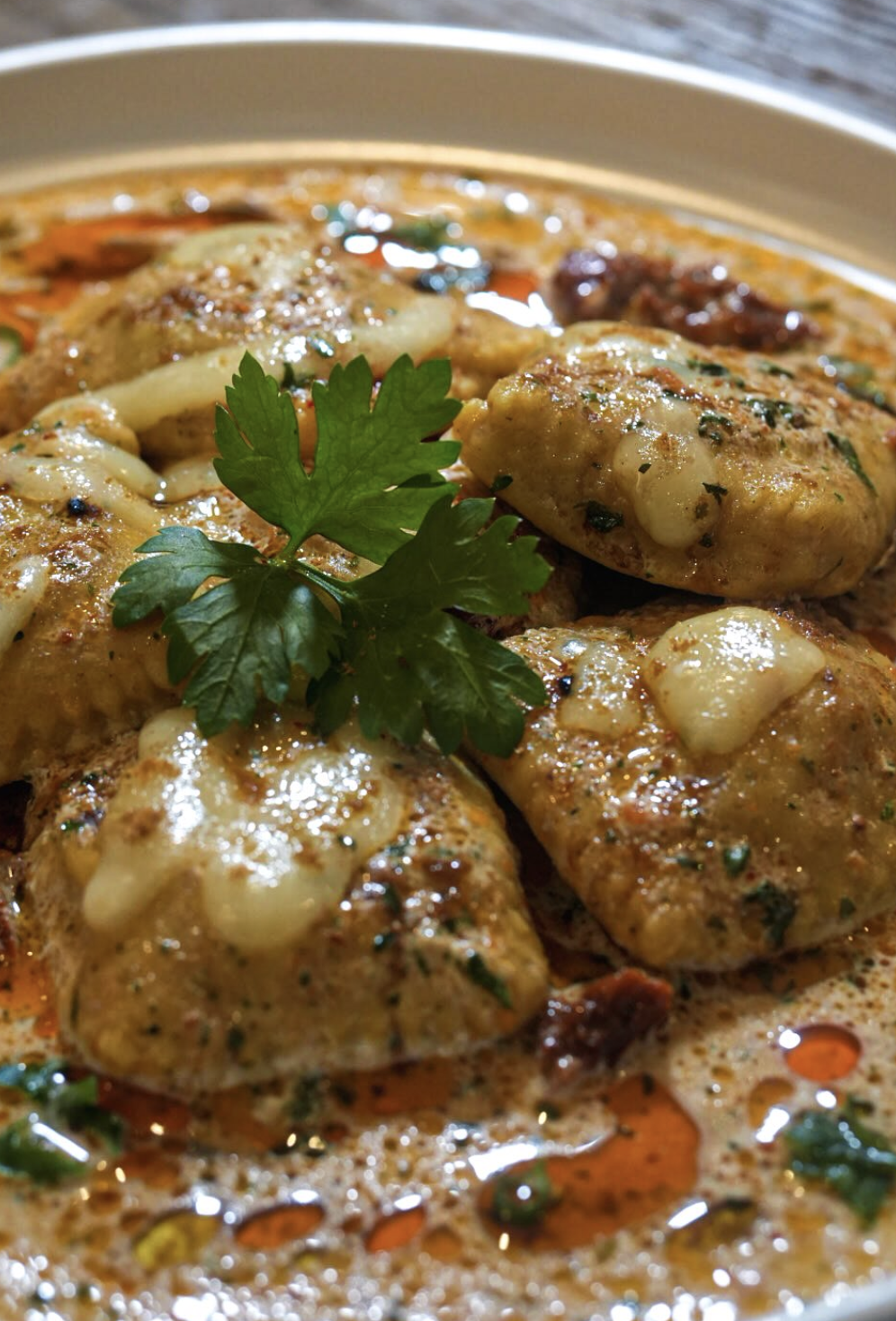 Wide plated view of creamy ravioli with parsley garnish and chili oil