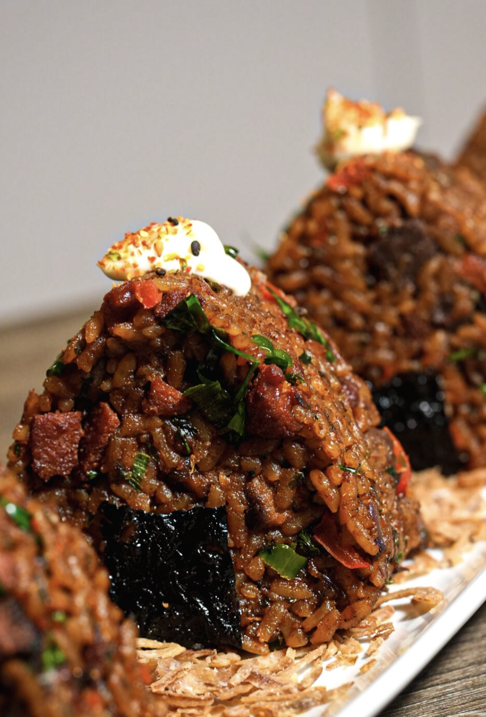 Lineup of molded jollof rice portions with beef, herbs, and cream garnish