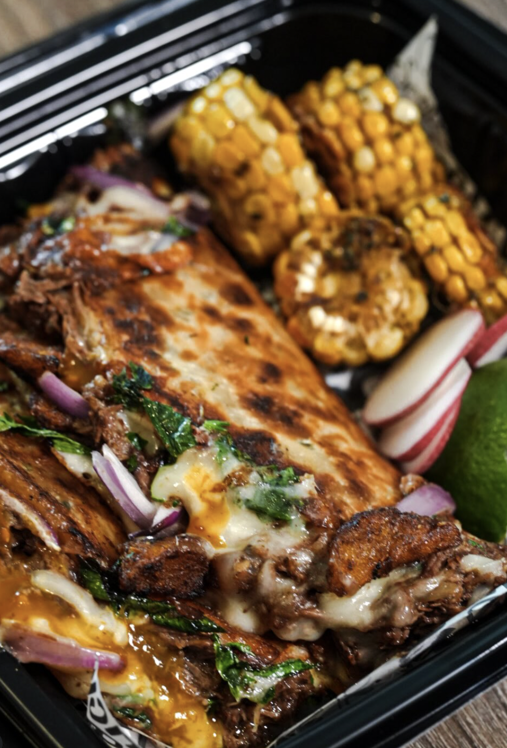 Cheesy folded quesabirria-style platter with roasted corn, radish, and lime