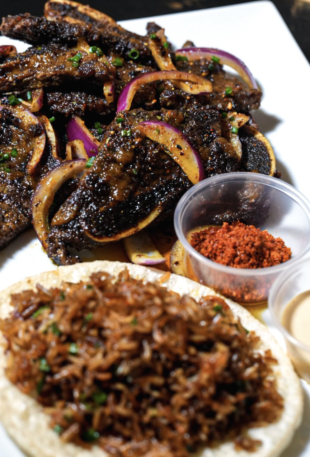 Suya beef platter with charred onions, spice, creamy sauce, and jollof rice in flatbread