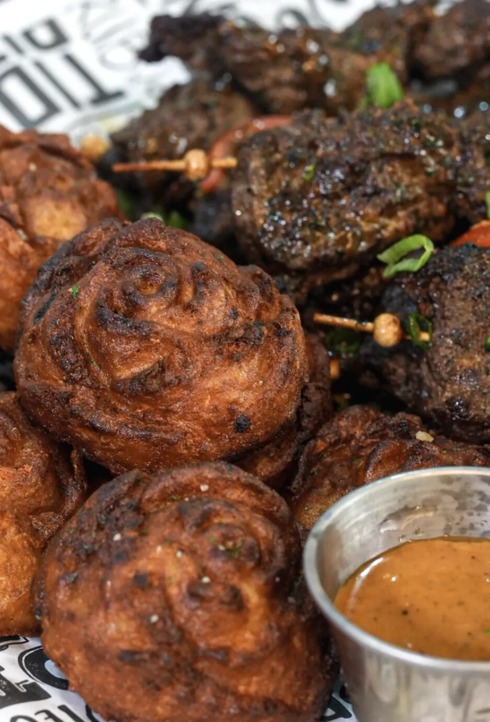 Close crop of puff puff and suya beef with orange dipping sauce