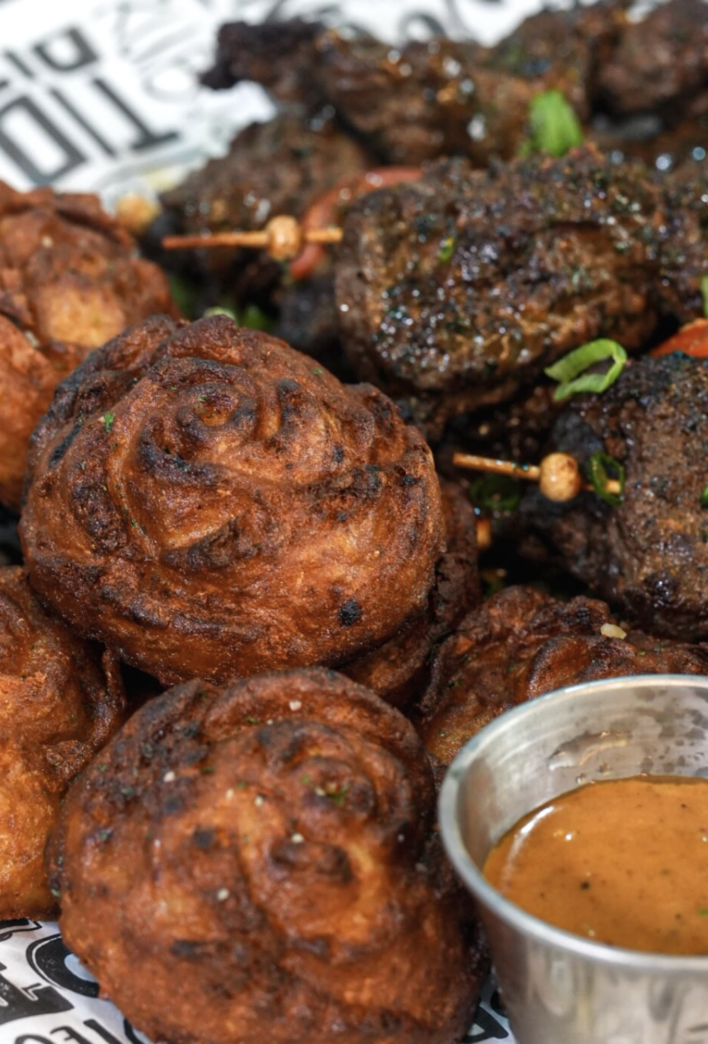 Close crop of puff puff and suya beef with orange dipping sauce