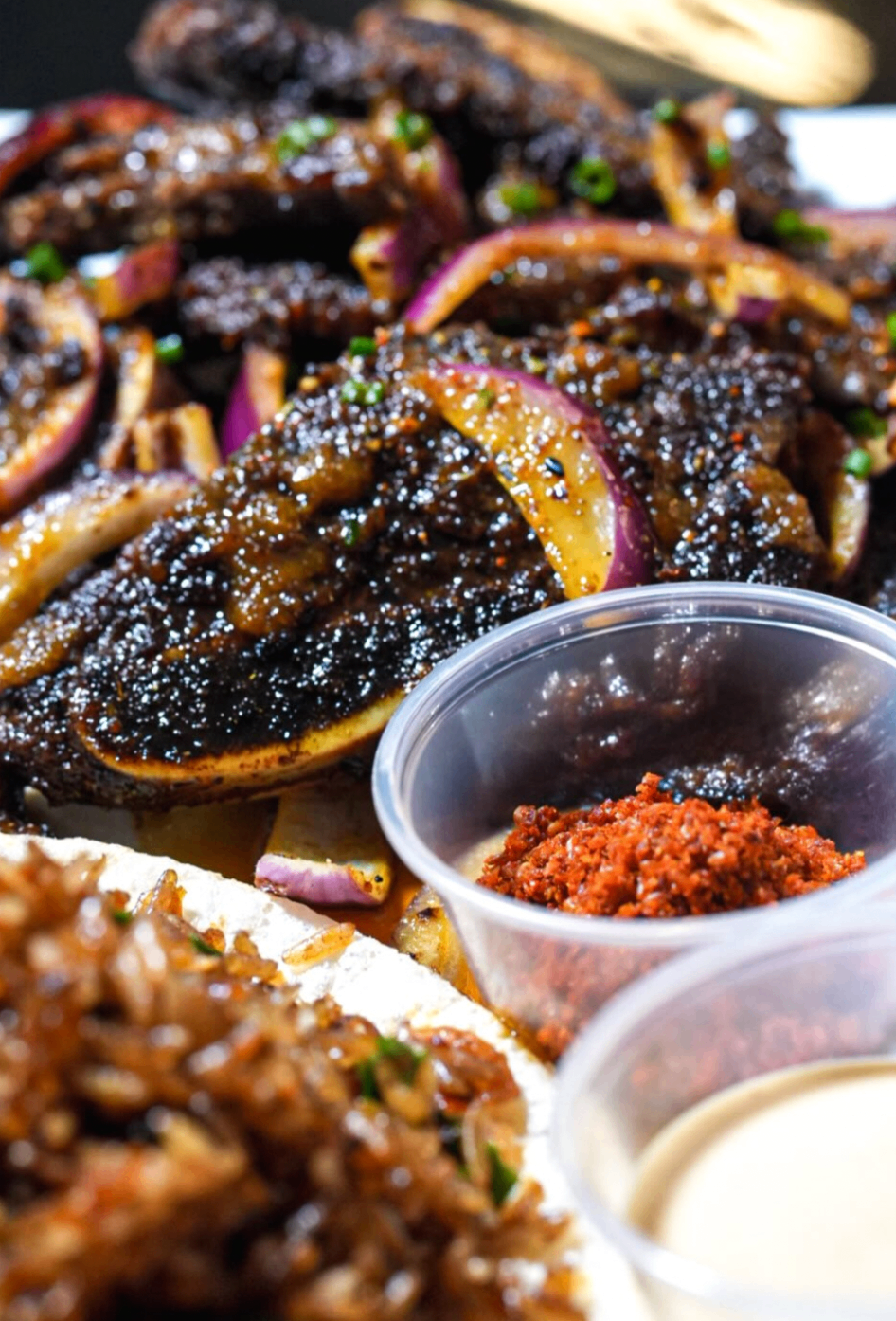 Detail of suya platter with spice cup, creamy sauce, and caramelized beef