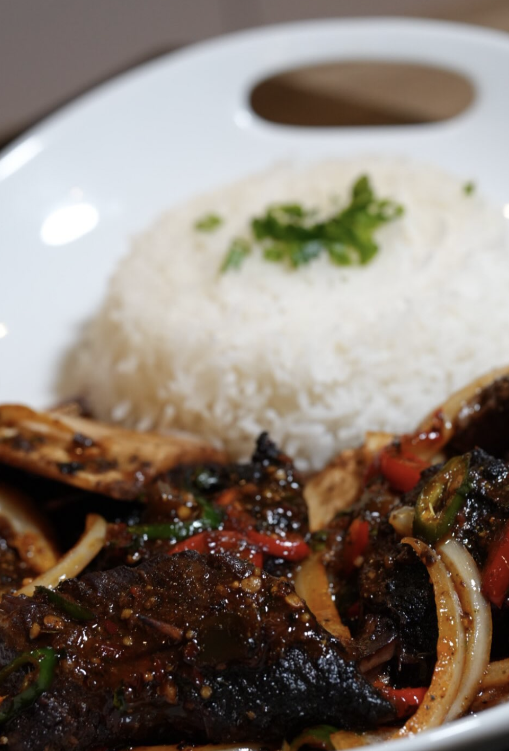 Plated braised beef and rice with fresh herbs on a white serving dish