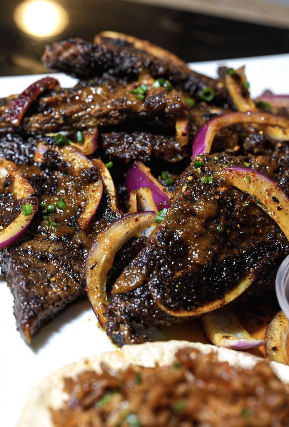 Charred lamb ribs with red onions, herbs, and rich glaze on a white platter